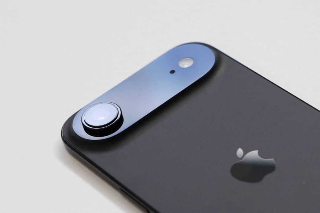 A imagem mostra a parte traseira de um smartphone, destacando a lente da câmera e o logotipo da Apple. O dispositivo é de cor preta e possui um design moderno, com uma lente circular e um pequeno sensor ao lado.