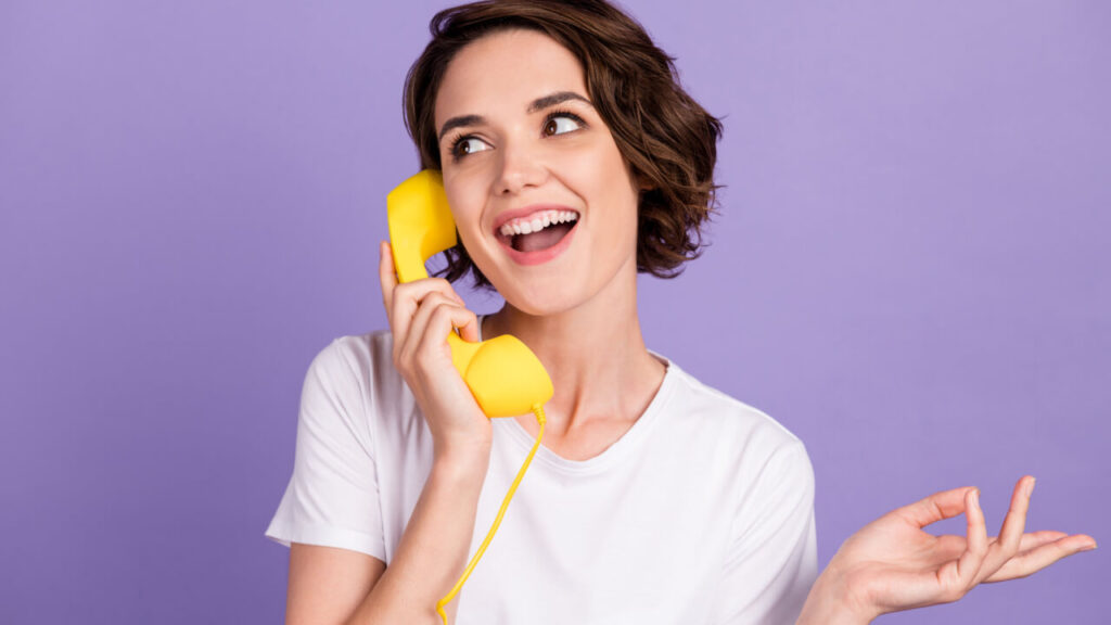 Mulher sorridente falando ao telefone em um fundo roxo.