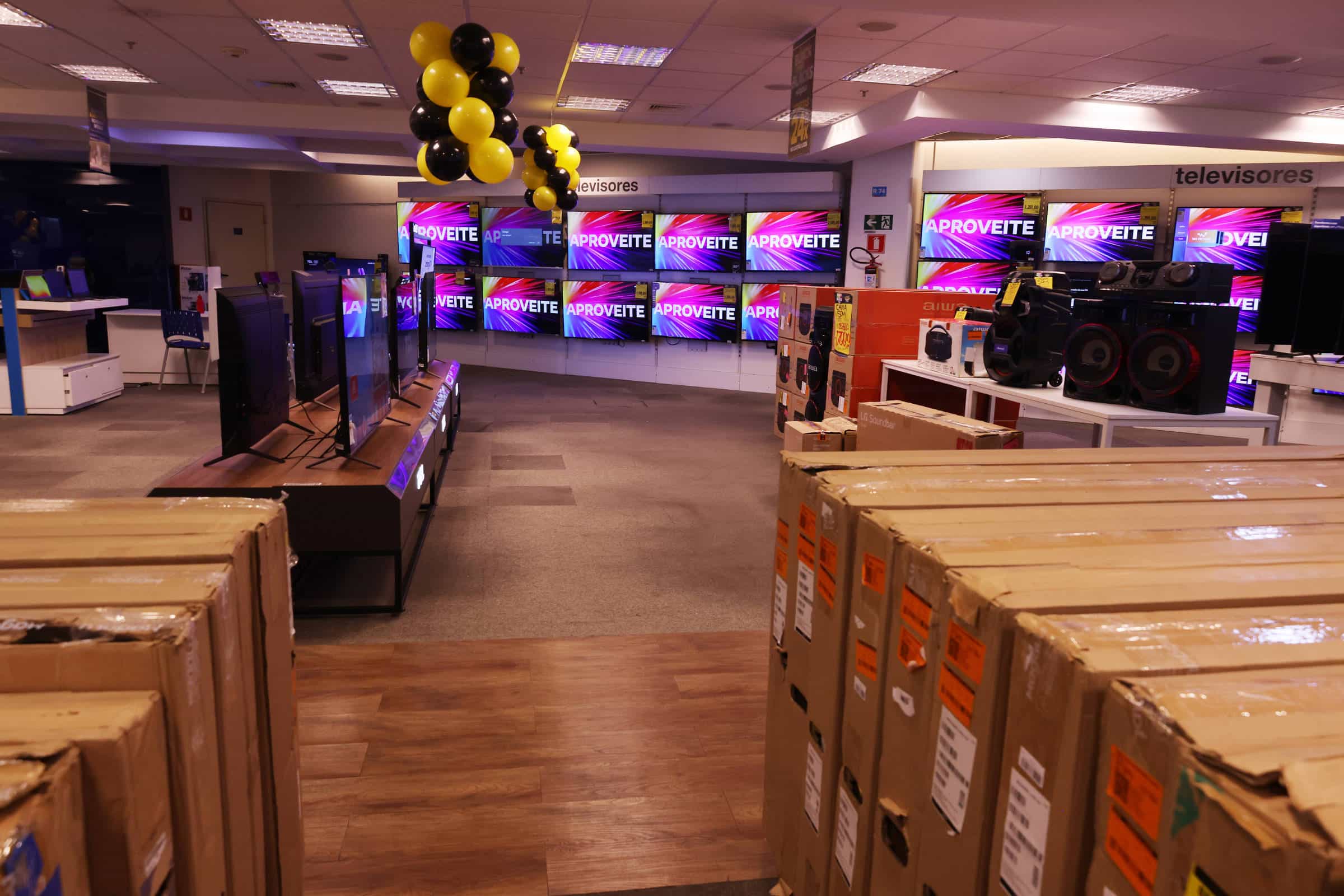 Interior de loja de eletrônicos com várias TVs ligadas exibindo a palavra