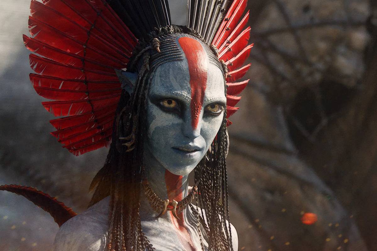 Mulher com pele pintada em tons cinza e branco, rosto marcado por pintura vermelha vertical central. Usa cocar alto com penas vermelhas e pretas e colar tribal. Fundo desfocado com luzes alaranjadas simulando faíscas.