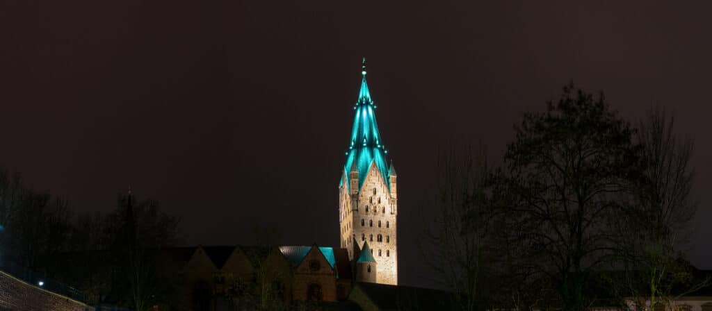 Der Turm des Paderborner Domes wird vor einem dunklen Nachthimmel farbig angestrahlt.
