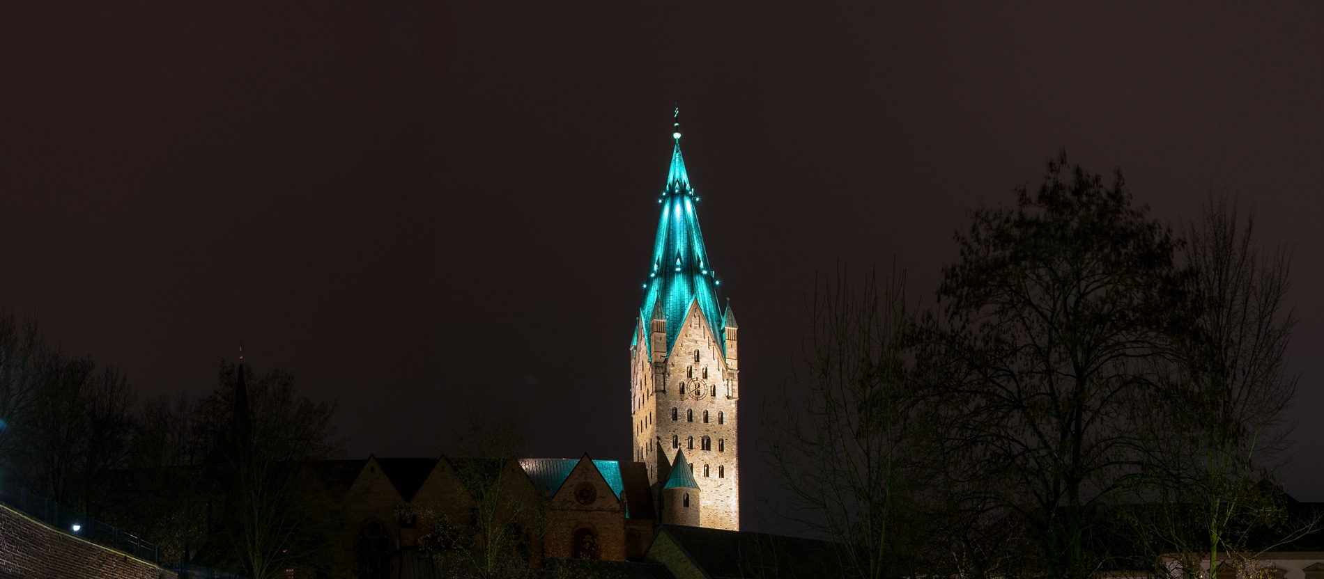 Der Turm des Paderborner Domes wird vor einem dunklen Nachthimmel farbig angestrahlt.