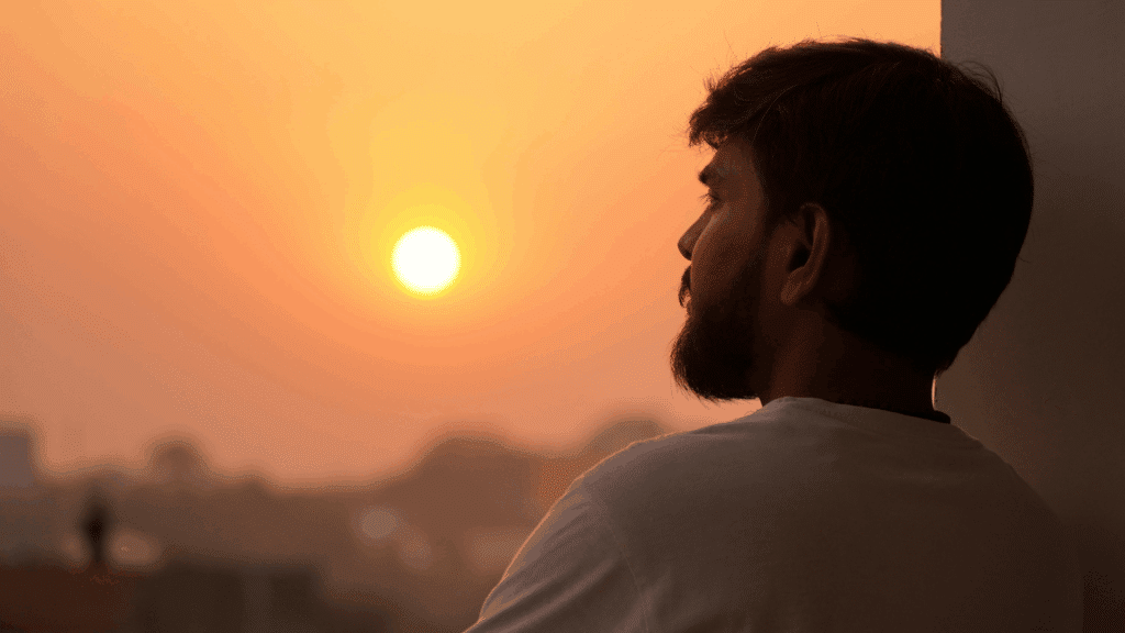 Um homem jovem observa o pôr do sol e está reflexivo.