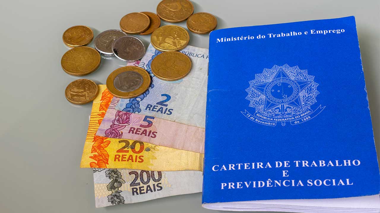 imagem de uma carteira de trabalho e ao lado notas e moedas em fundo cinza