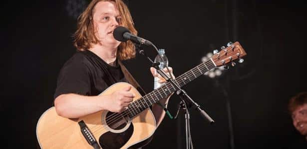 Cantor Lewis Capaldi no palco com violão e próximo ao microfone