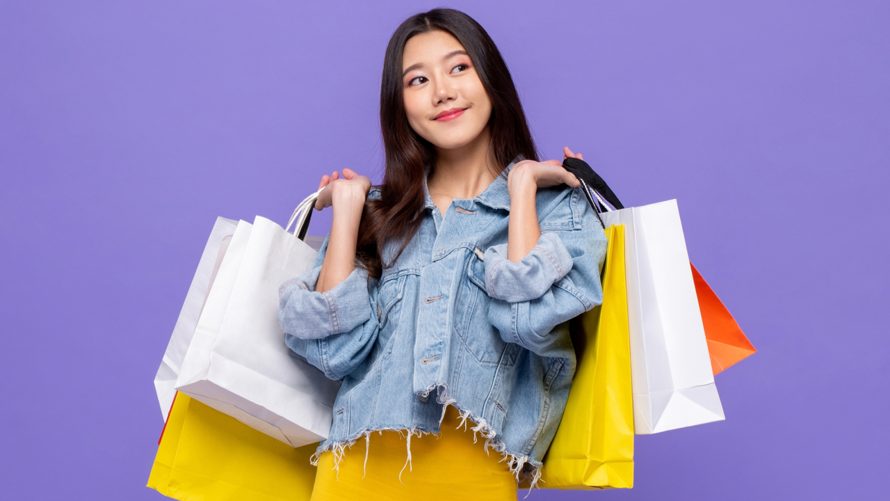 mulher carregando muitas sacolas de compras e sorrindo em fundo roxo