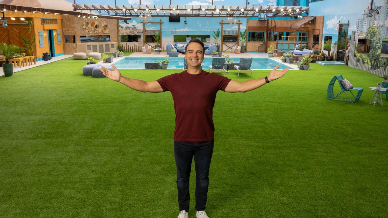 Mostra Tadeu Schimidt no gramado do BBB. Homem branco, cabelo preto curto, camiseta vermelha e calça preta.