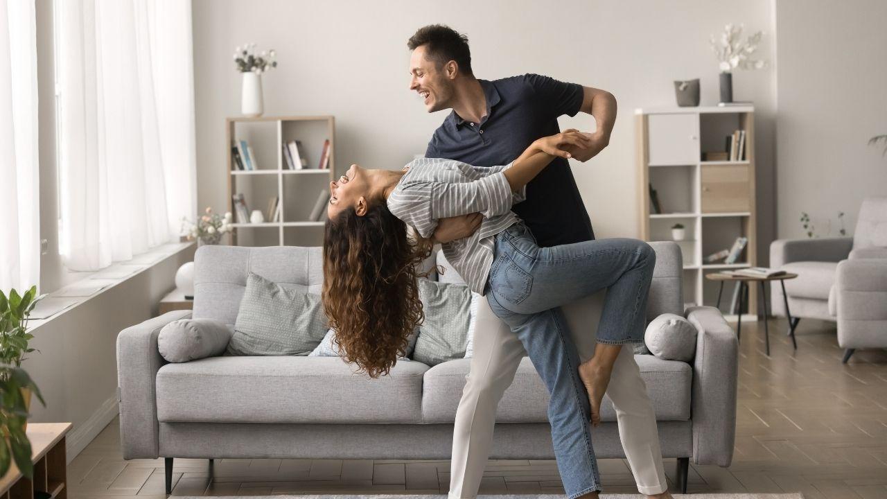 Homem abraçando a mulher numa sala de casa.