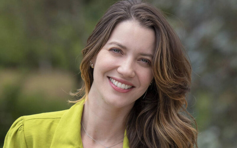 Em foto colorida, mulher de calça jeans e jaqueta verde posa para foto