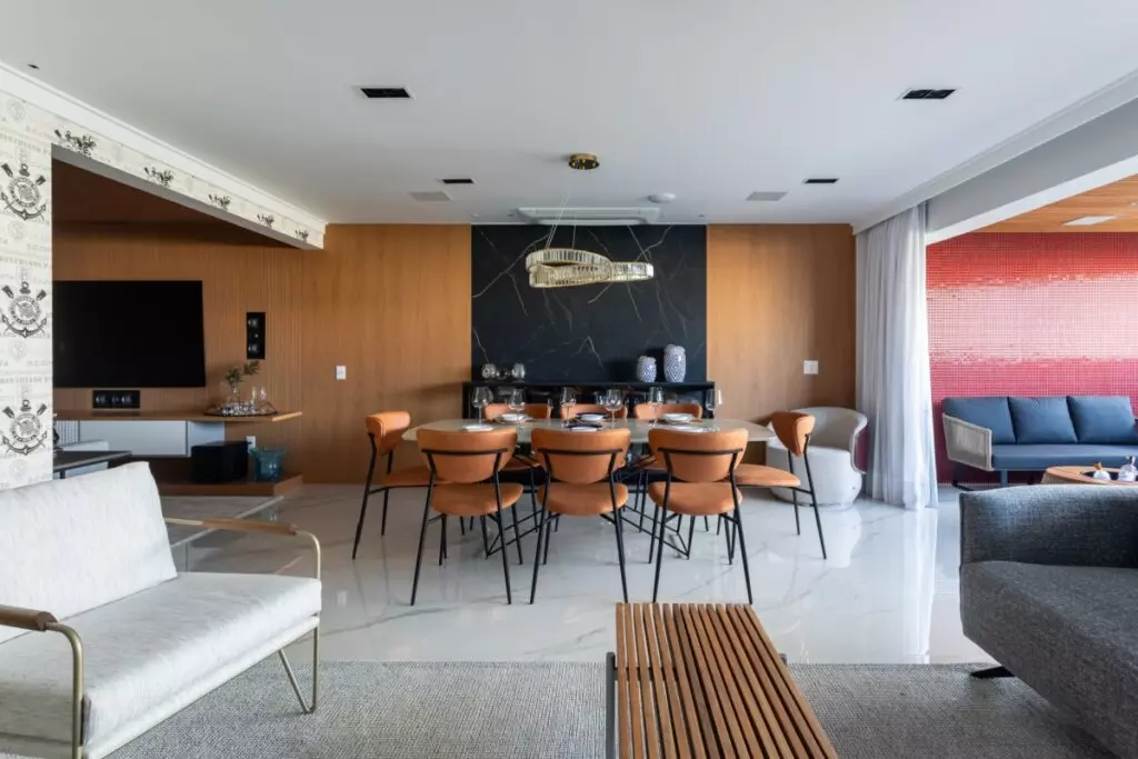 Sala de estar integrada à sala de jantar com mesa central, cadeiras, painel de madeira e área de estar ao fundo