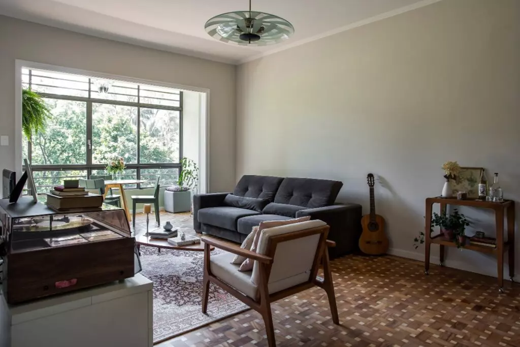 Sala de estar com sofá, poltrona, mesa lateral, instrumentos musicais e janela ao fundo