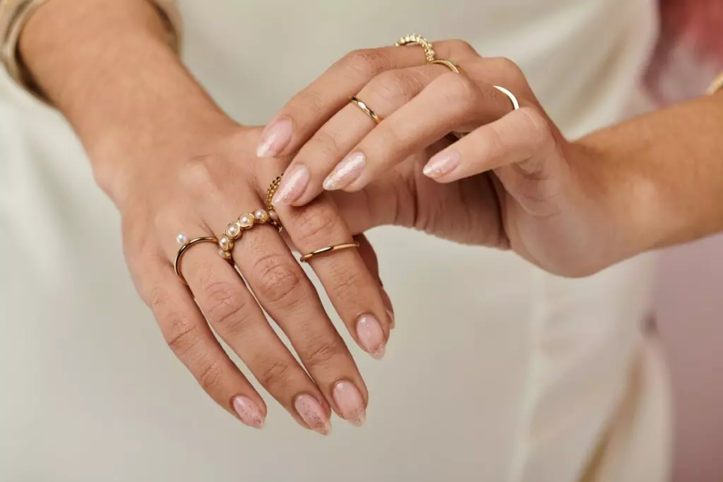 duas mãos femininas com unhas claras e anéis dourados nos dedos
